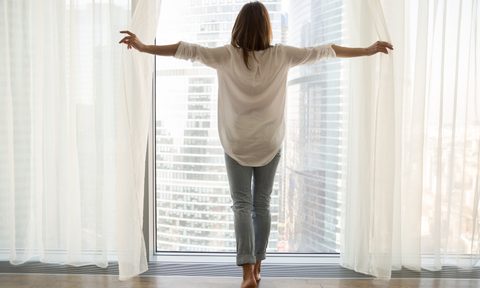 woman opening sheer curtains