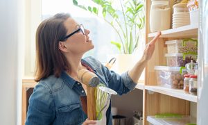 Woman with cooking accessories in kitchen interior, background wooden shelf in pantry with utensils, food cans