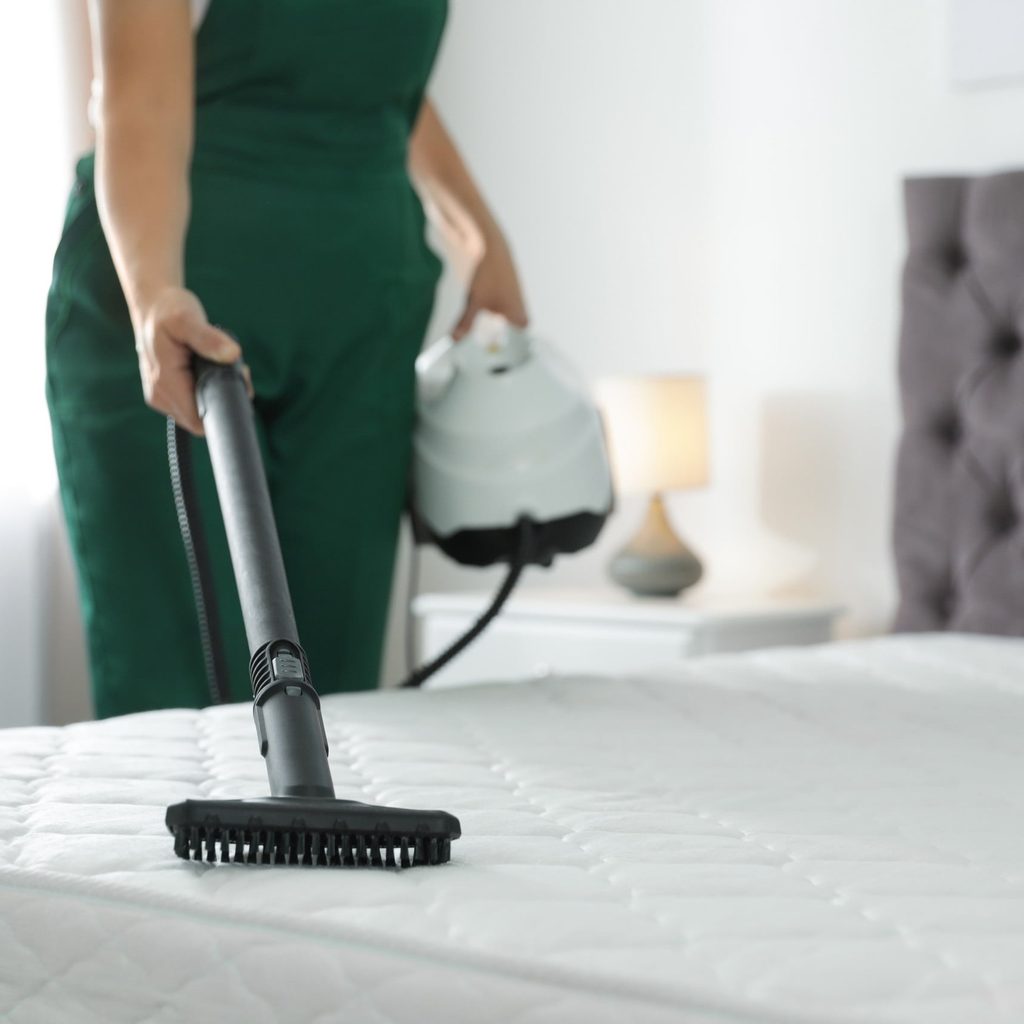 Woman vacuuming mattress with brush attachment