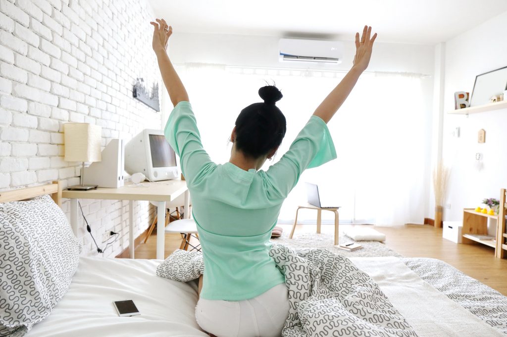 woman stretching in bed with ac unit on wall