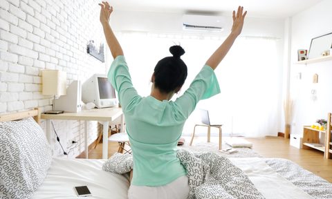 woman stretching in bed with ac unit on wall