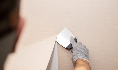 man using a scraper to tear wallpaper from the wall