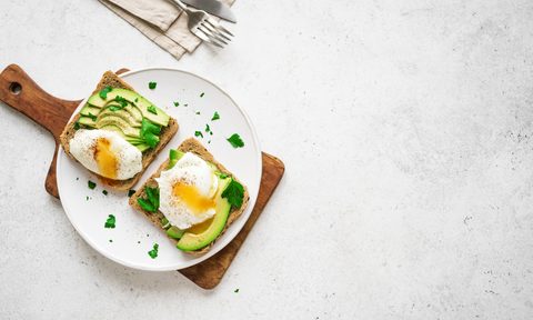 Avocado toast with eggs on white plate and table