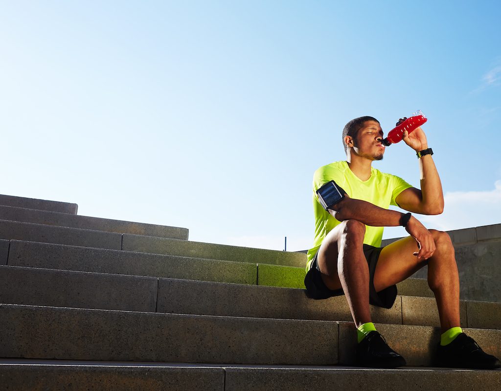 Runner seated on the steps drinking a sports drink