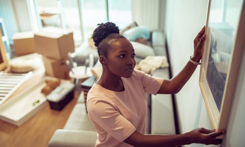 woman hanging picture on wall with boxes in background