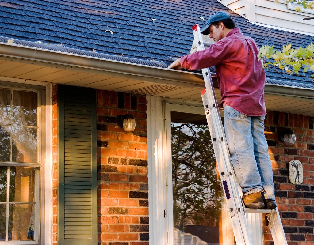 man on a ladder cleaning rain gutters