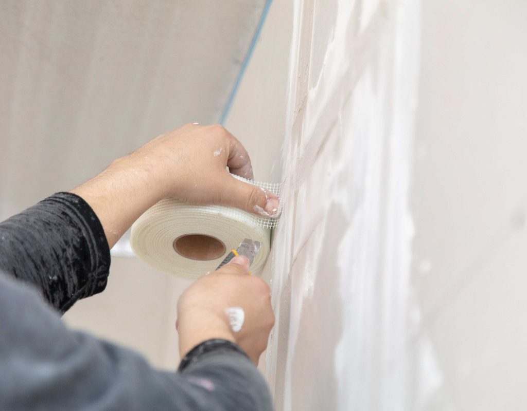 Person using drywall tape to repair drywall