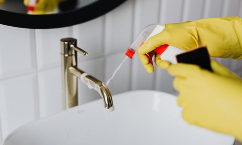 cleaning bathroom sink with spray and yellow gloves