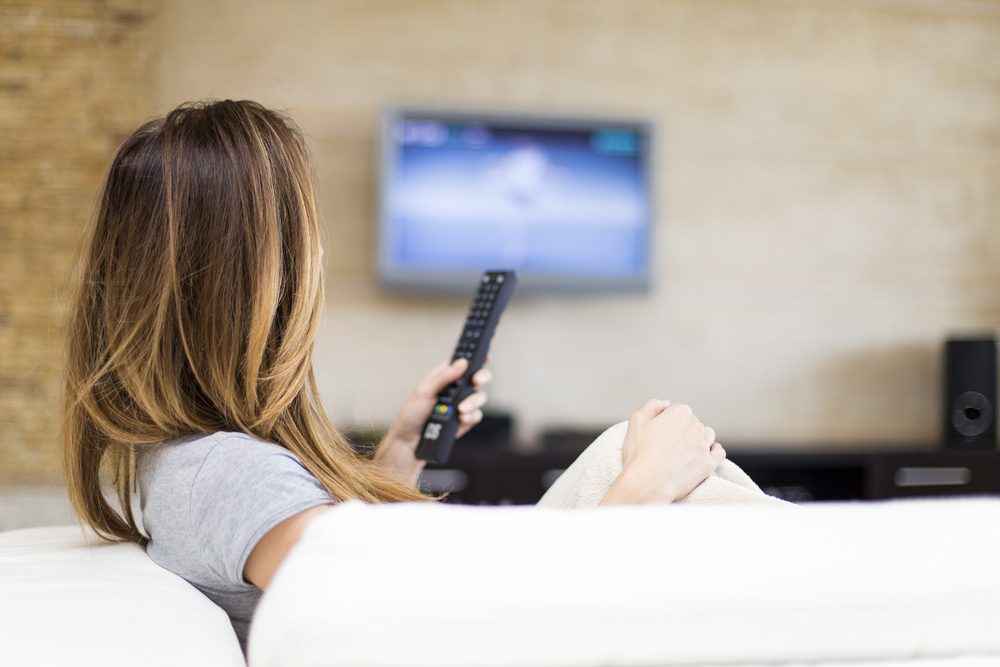 woman with remote watching tv on couch