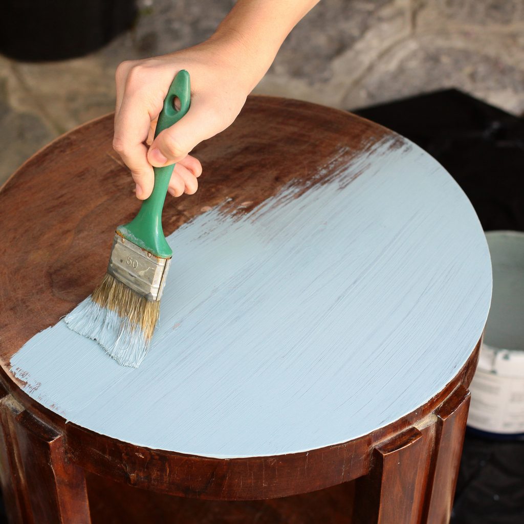 Woman's hand staining a stool with paintbrush