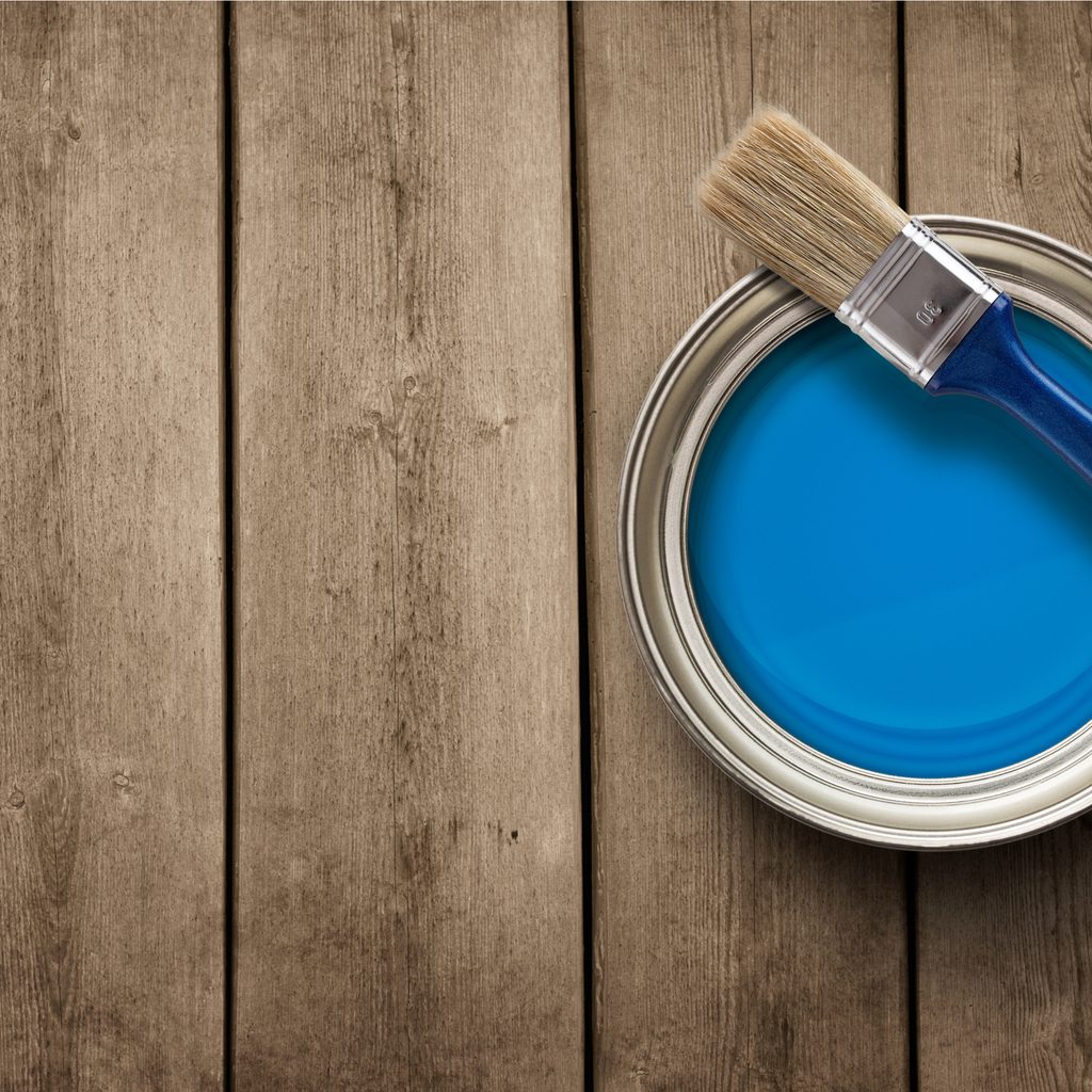 Small blue paint can with paint brush set on top.