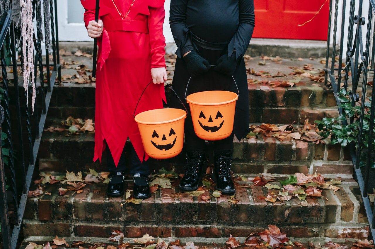 two children from the neck down in costume with trick or treating bins