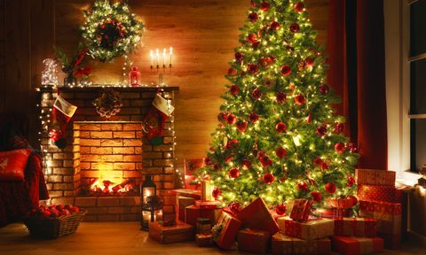lit christmas tree with presents under it next to a fireplace