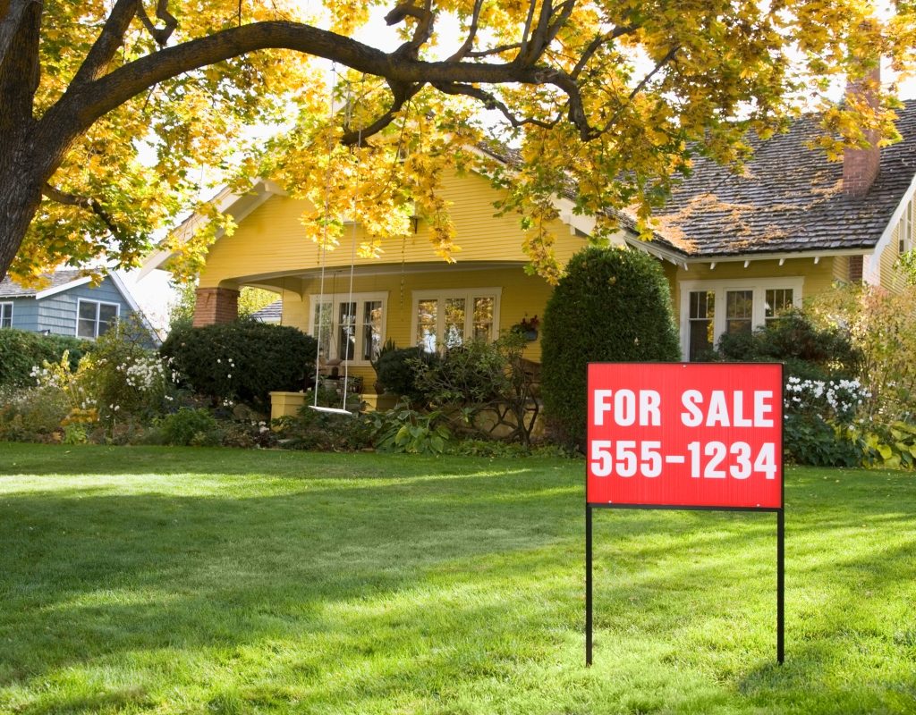 For sale sign in front yard of suburban home