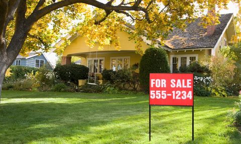 For sale sign in front yard of suburban home