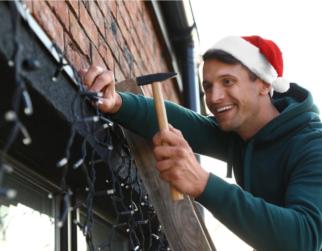 Man attaching Christmas lights around a window