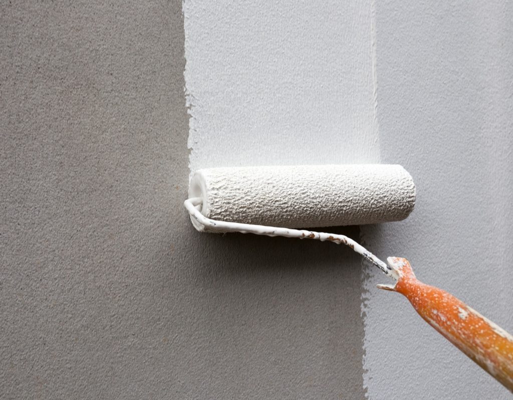 person using paint roller to paint grey wall