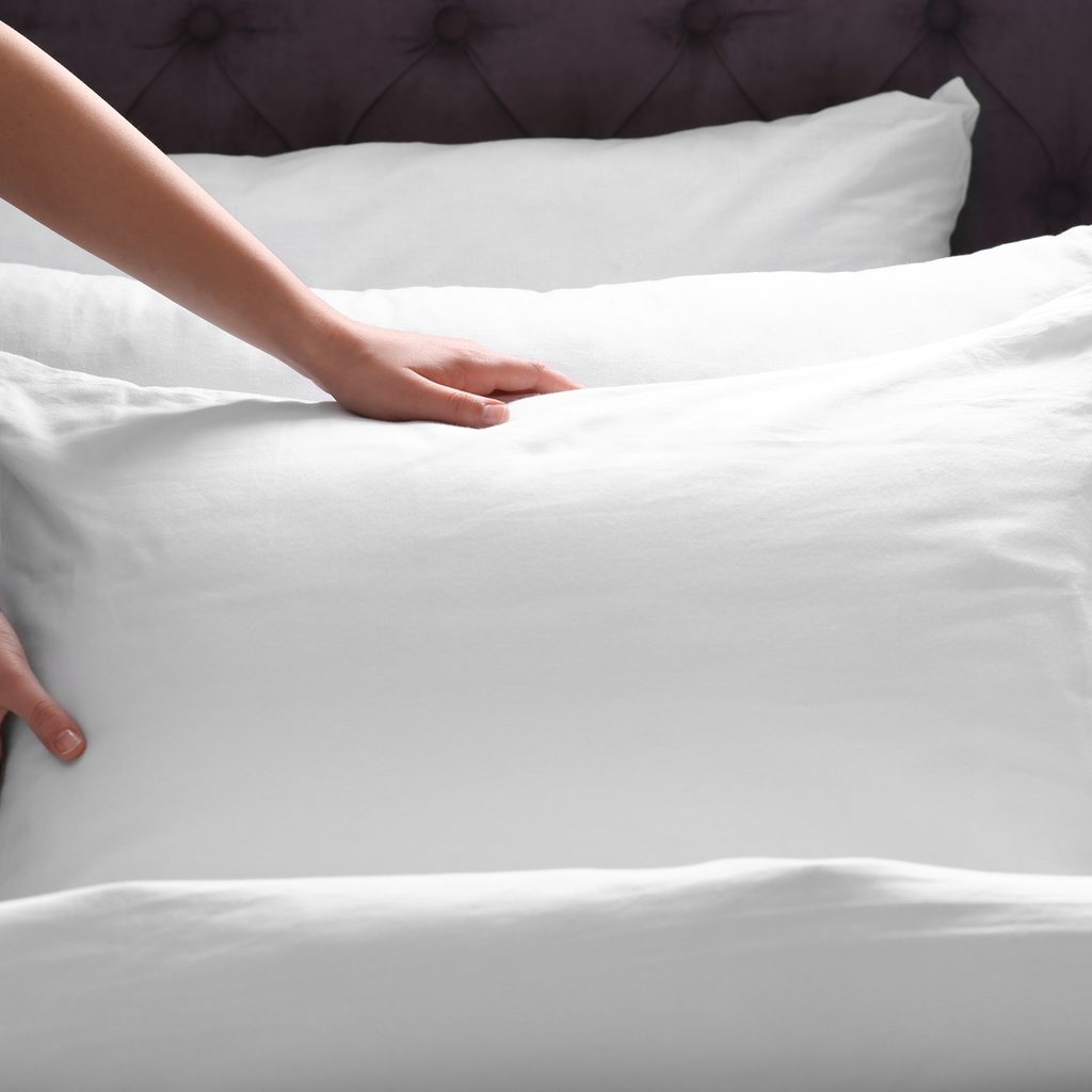 person fluffing pillow on the bed