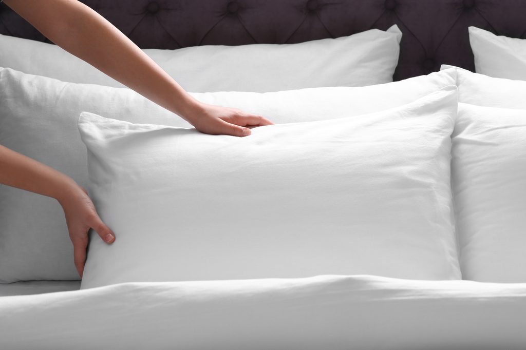 Person fluffing a pillow on the bed