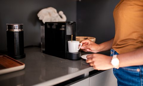 person using a compact coffee maker on kitchen counter