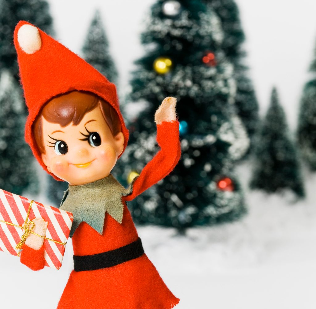 Old fashioned elf in front of Christmas trees.