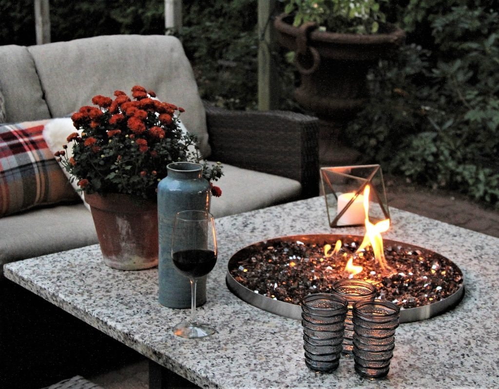 Outdoor propane gas fire pit with fall flowers and drinks