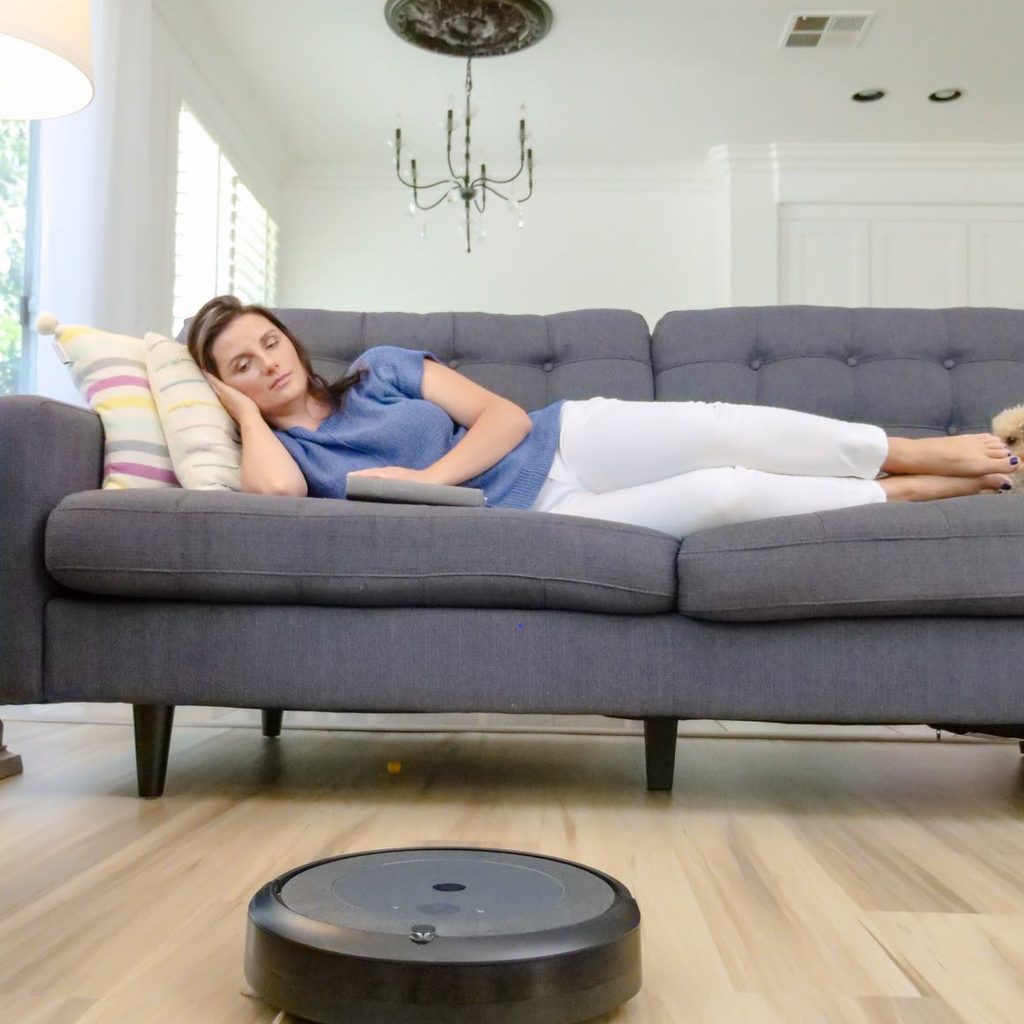 woman lying on couch while robot vacuum cleans