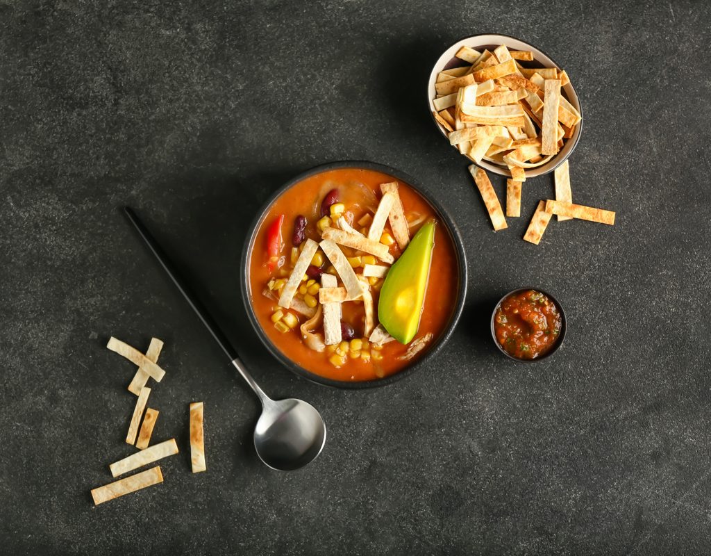 A bowl of chicken tortilla soup and some bowls of garnishes.