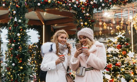 Two women holiday shopping. one is looking at her phone