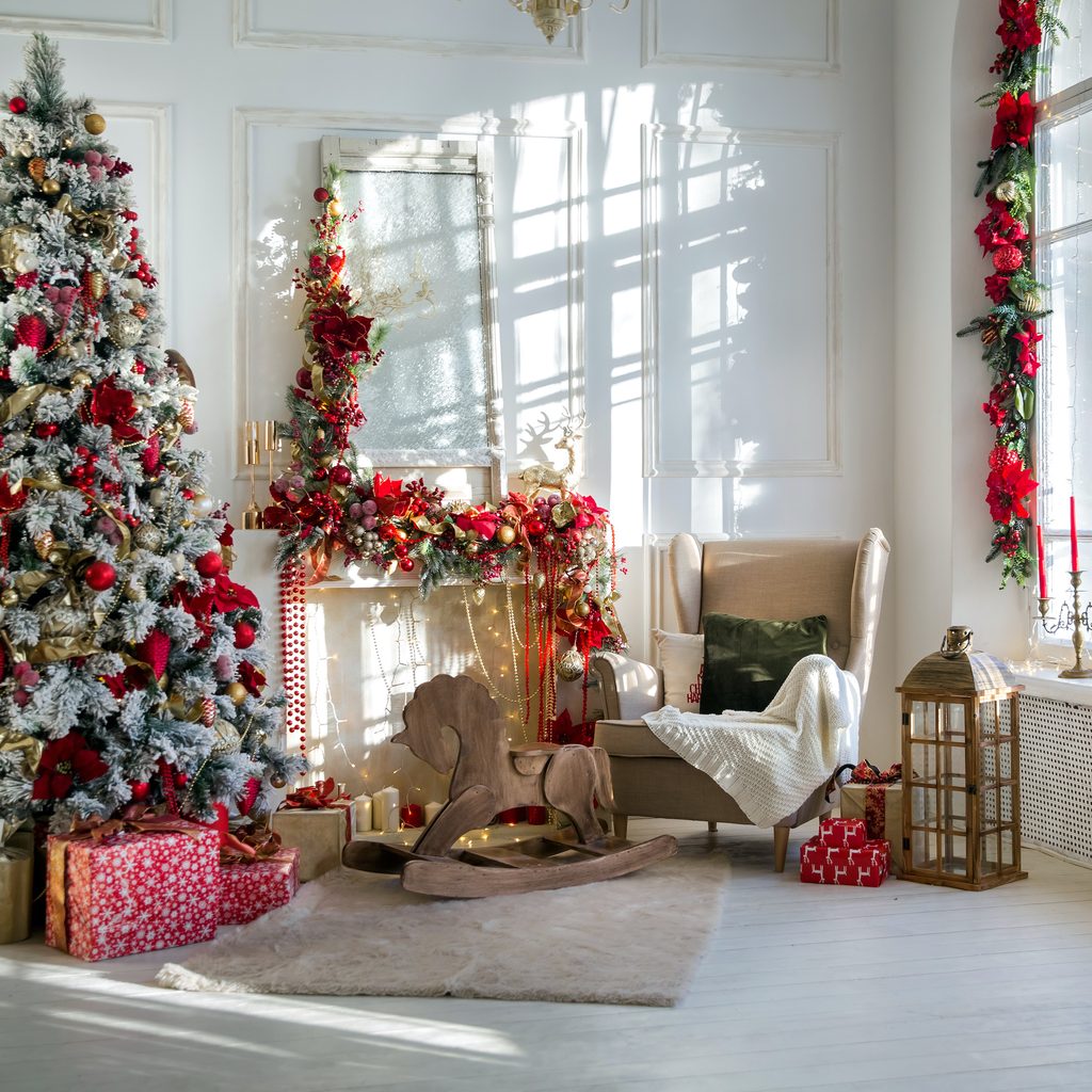 White room interior in red tones with New Year tree decorated, present boxes and artificial fireplace