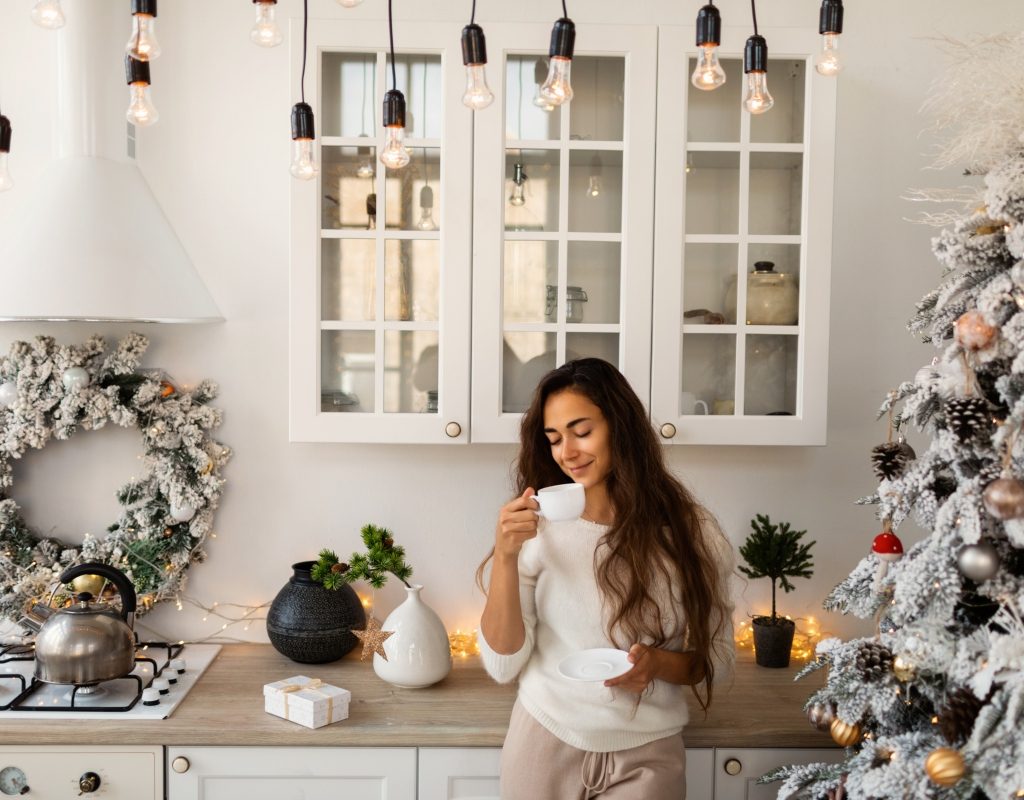 Woman drinking coffee in rustic kitchen with a Christmas tree