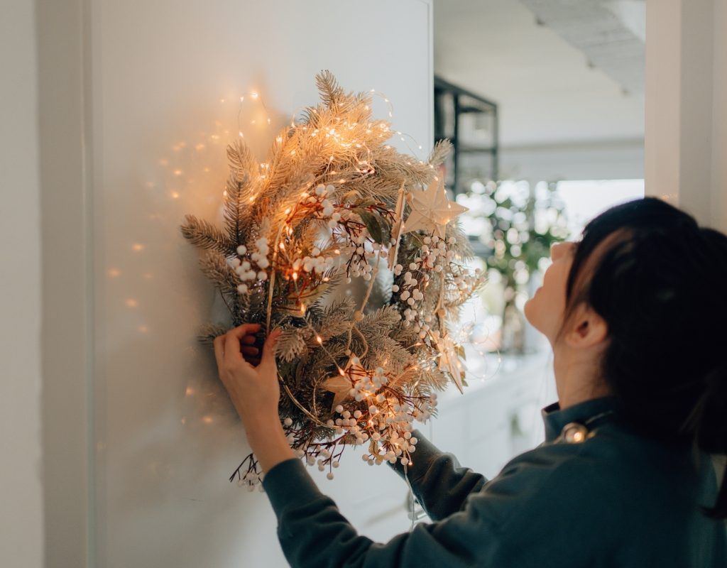 Woman putting up a white and tan winter wreath