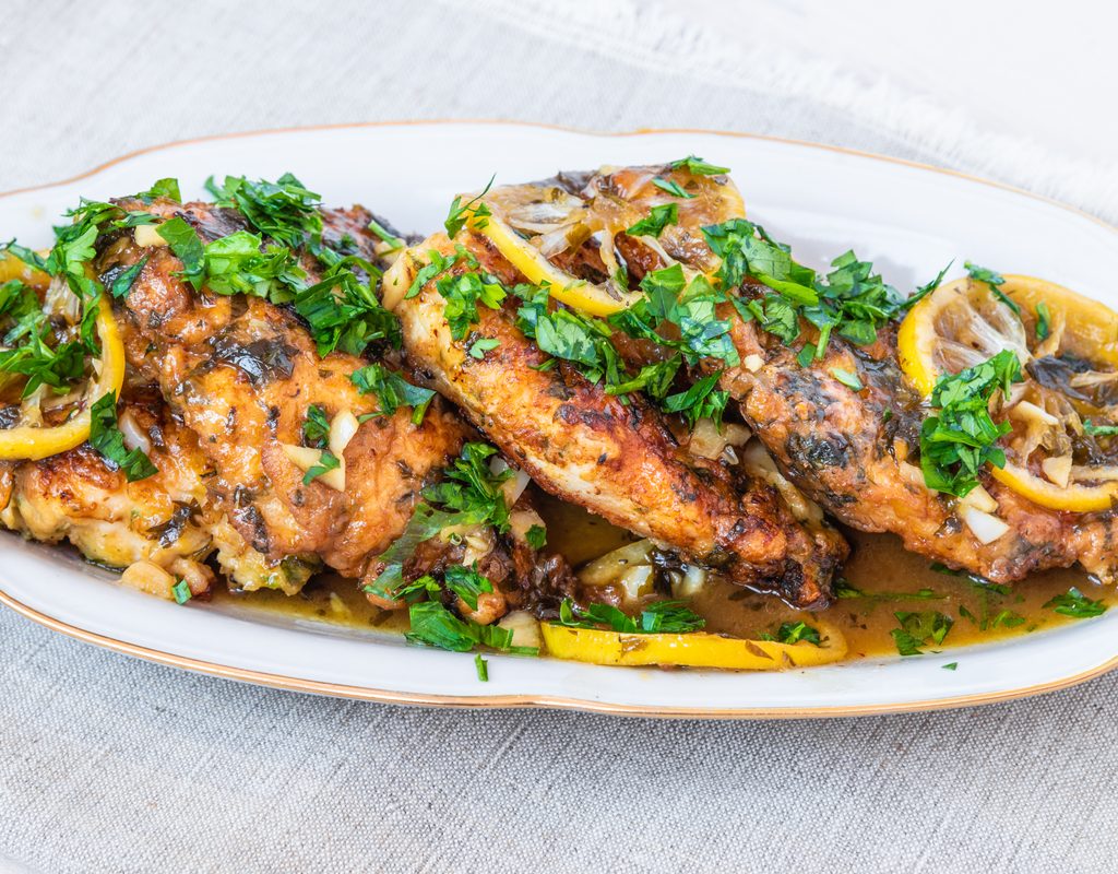 Cooked chicken breasts with lemon and parsley on a white plate