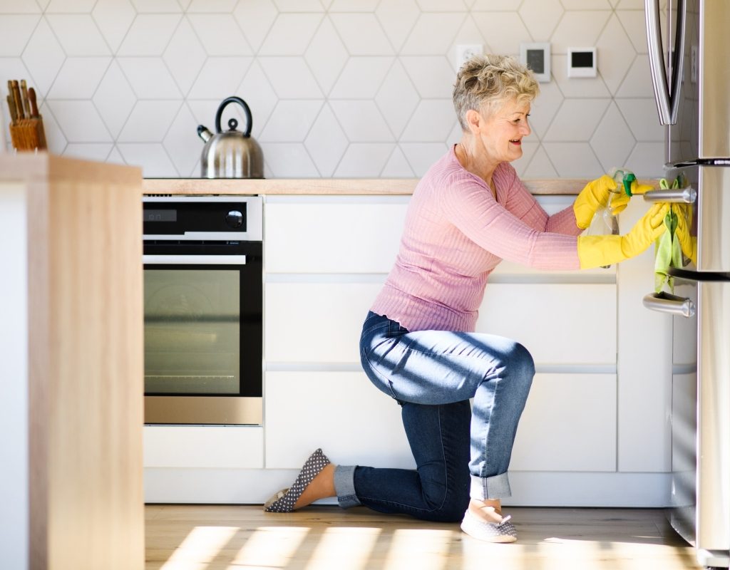 an elderly woman disinfects and cleans the refridgerator