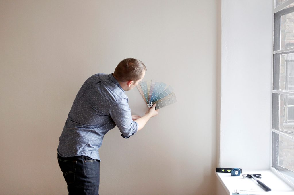 Man comparing paint swatches to greige walls.