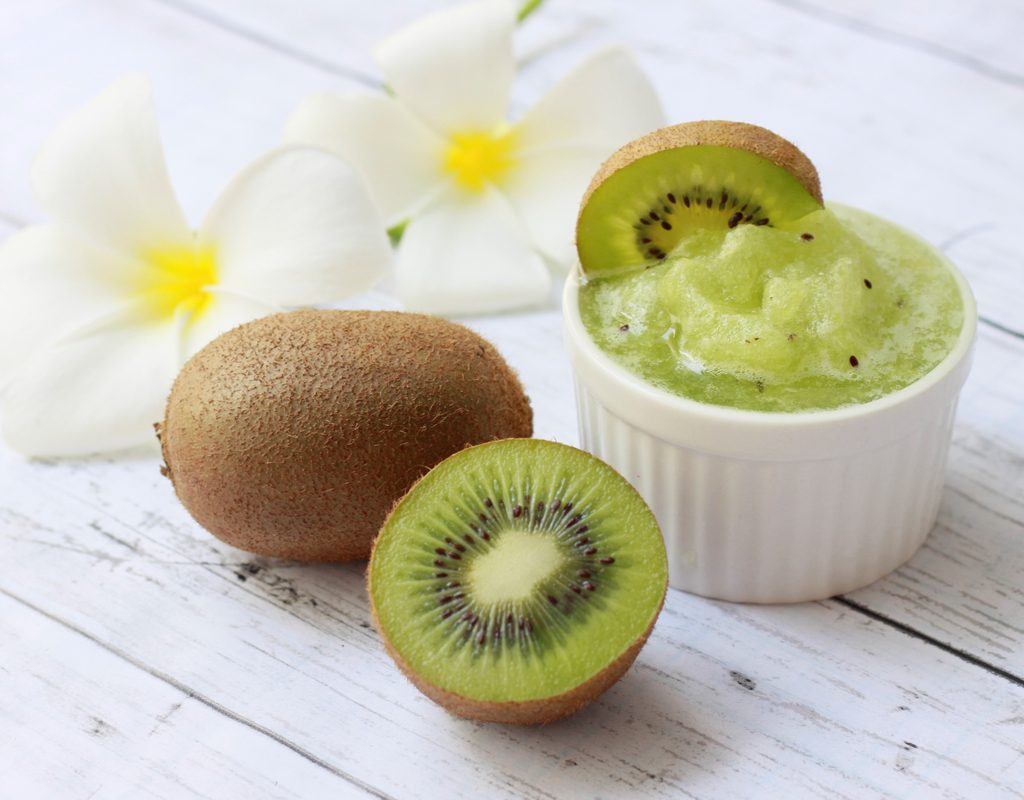Fresh kiwi fruits sorbet in white bowl with fresh kiwi on wooden background