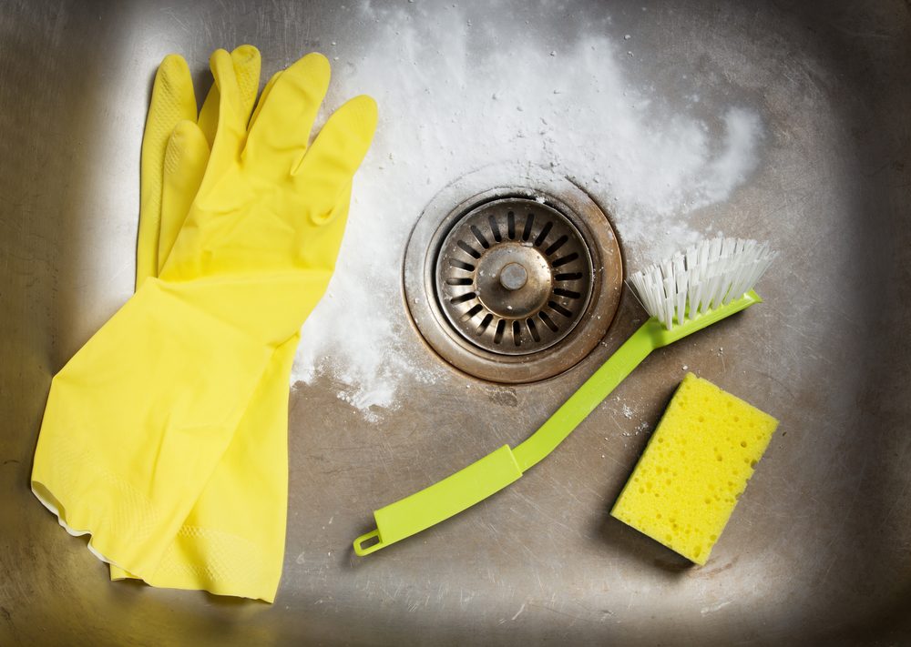 Rubber gloves, scrub brush, and sponge in a kitchen sink.