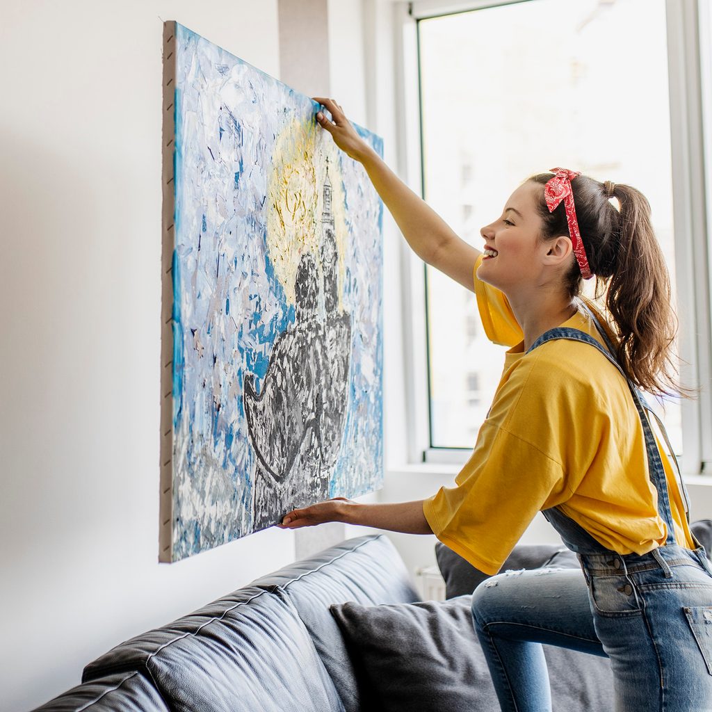 Woman hanging art on wall behind couch