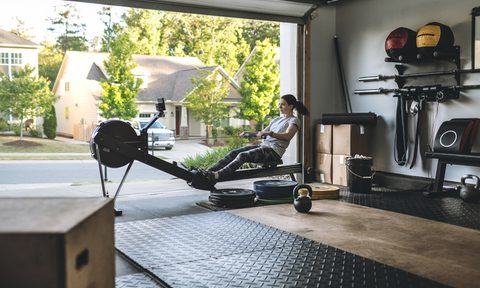 garage gym remodel active woman exercising on a rowing machine in her home during covid 19 pandemic