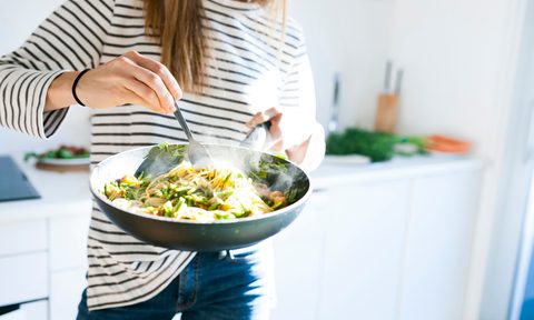 Young woman holding pan with vegan pasta dish
