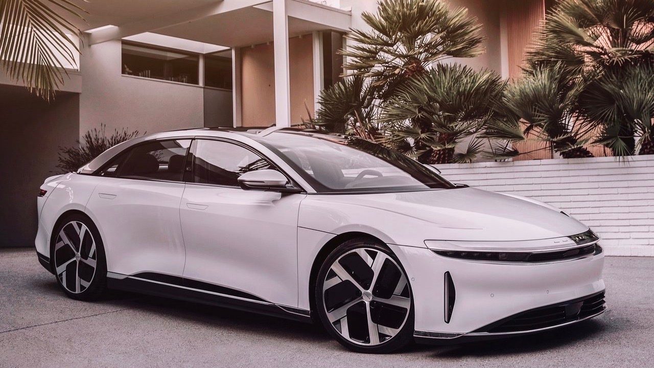 Three quarters front view of a white Lucid Air parked in a modern house's driveway.