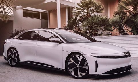 Three quarters front view of a white Lucid Air parked in a modern house's driveway.