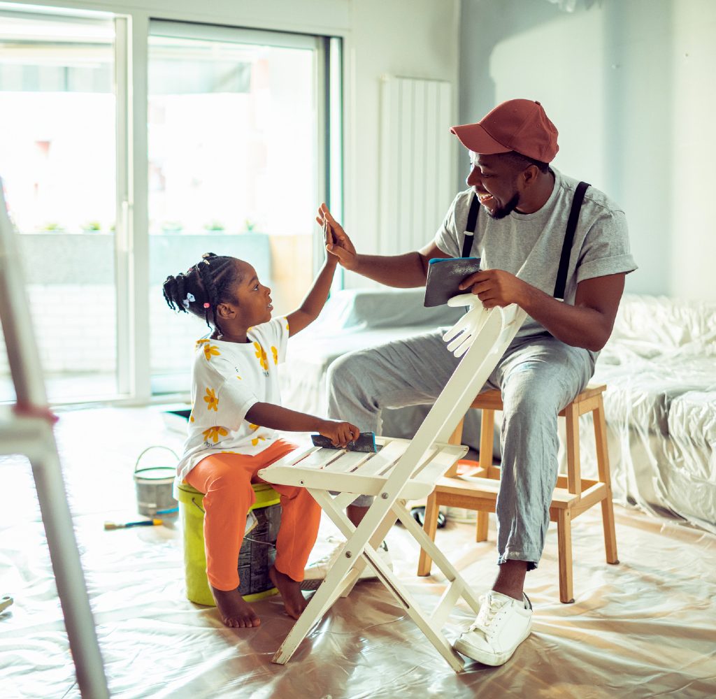 Man and child painting chair inside.