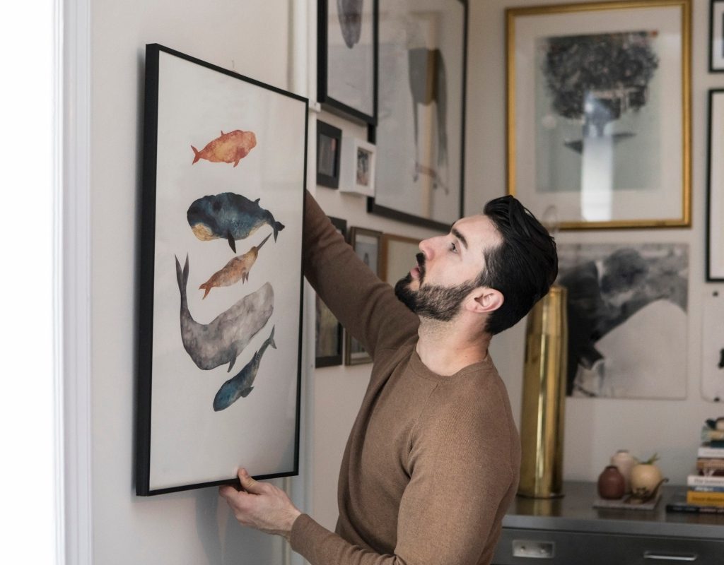 man hanging artwork in his home for his design scheme