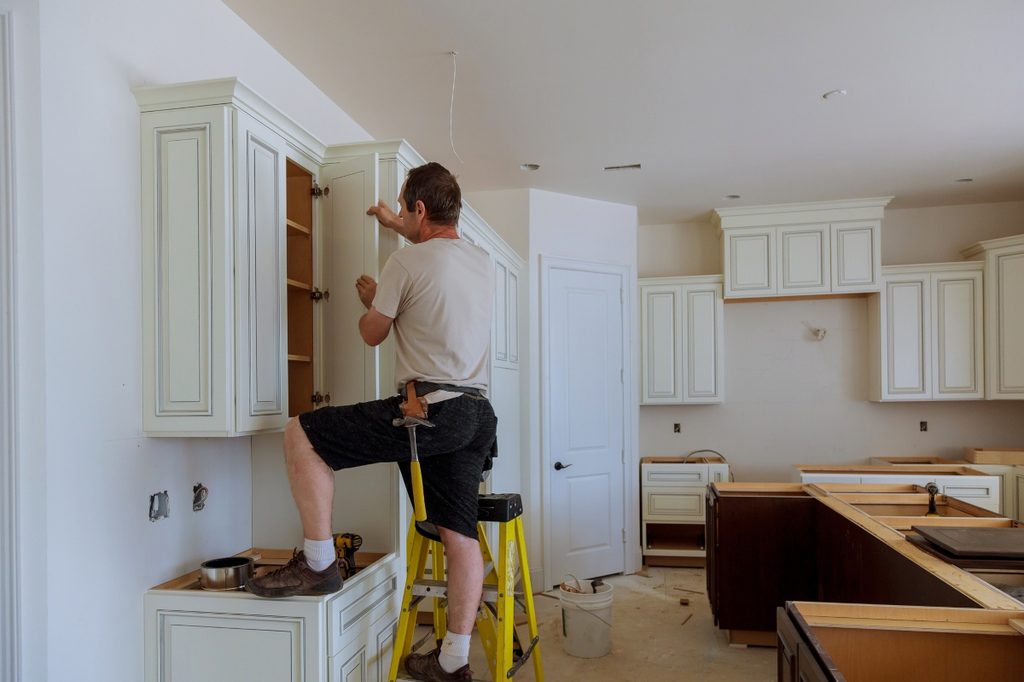 man installing white kitchen cabinets