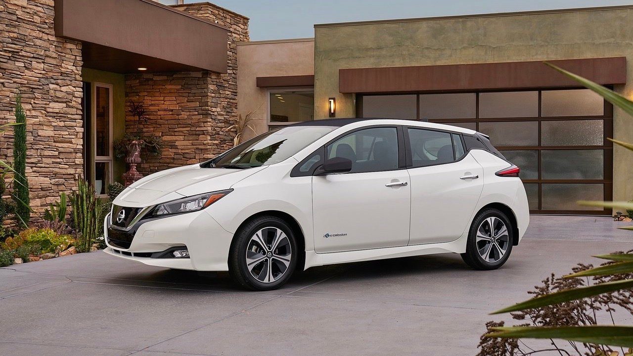 Three quarters front view of a Nissan Leaf parked in a modern house's driveway.