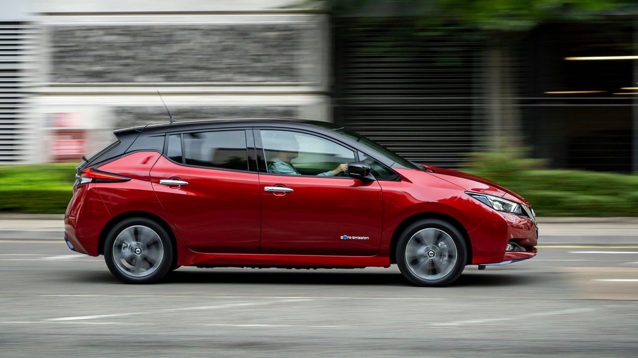 Side view of a moving red NIssan Leaf.