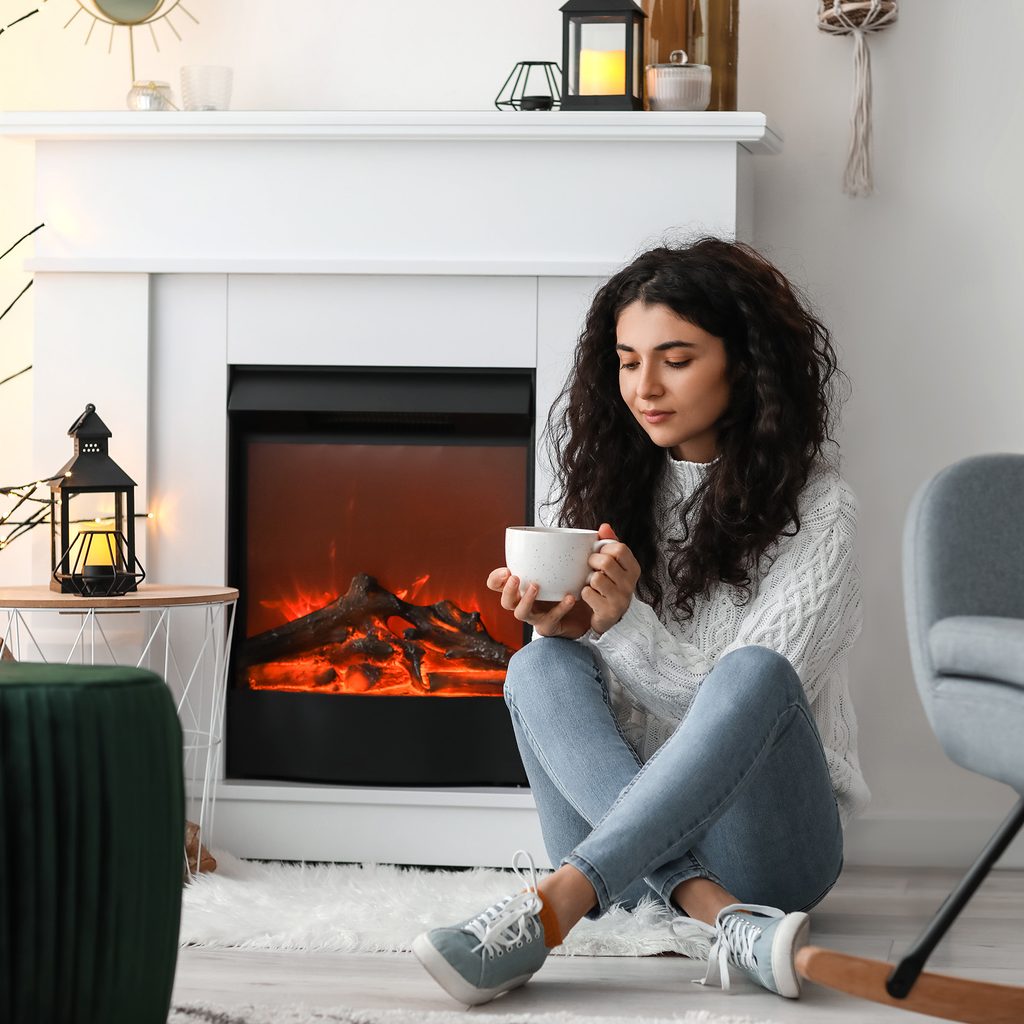 Woman sitting by electric fireplace with mug