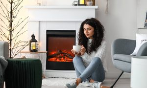 Woman sitting by electric fireplace with mug