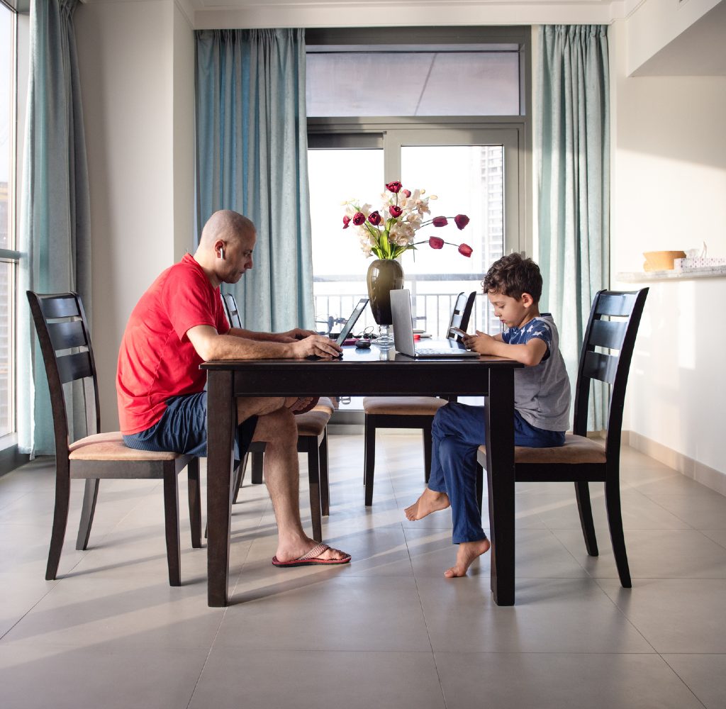 Dad and son on computers at dining room table.